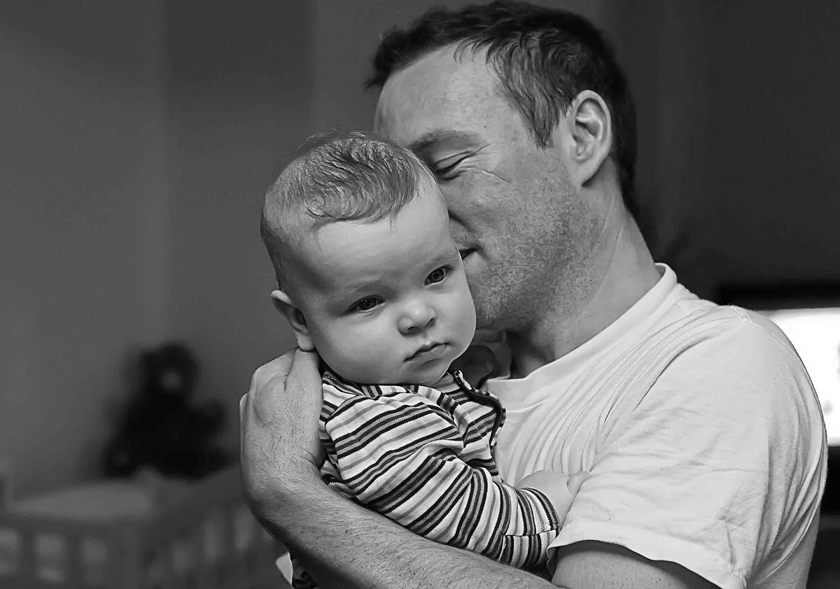 Father holding his baby son close with his eyes closed